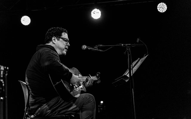 Black and white image of musician performing on stage with guitar