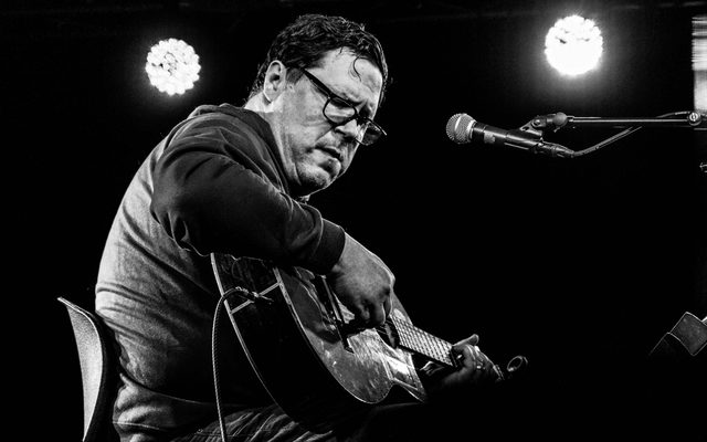 Black and white image of musician performing on stage with guitar