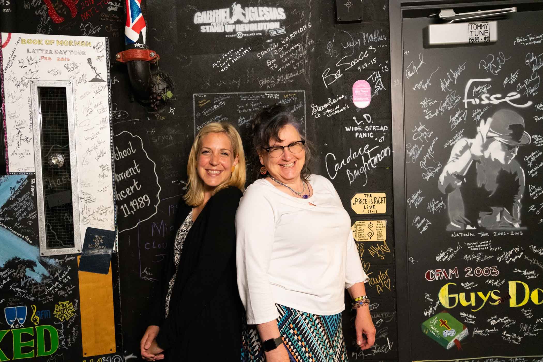 Jen Cumberworth and Louse Thomas-Vails standing near an autographed wall