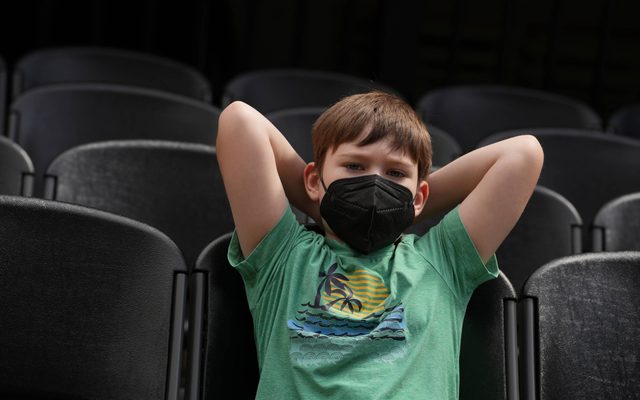A young boy seated with a mask on