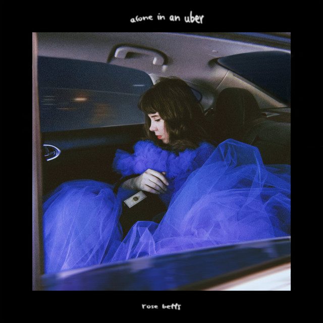 Picture of a woman in a dress sitting inside car with text ALONE IN AN UBER ROSE BETTS