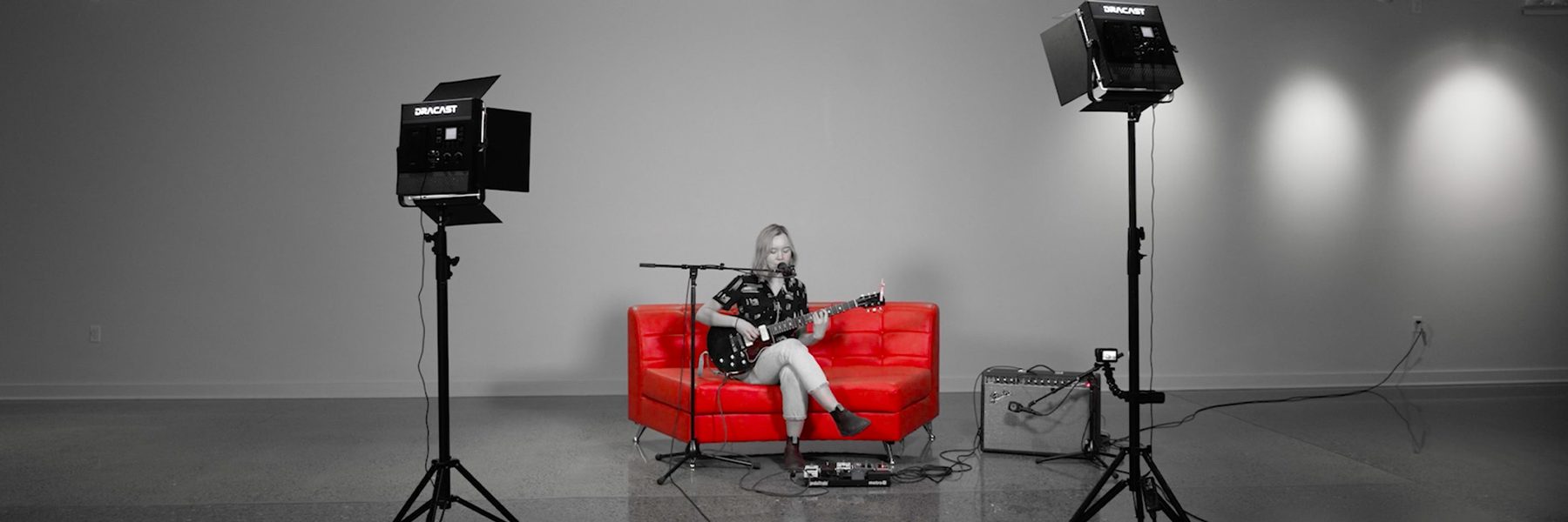 black and white image of a woman singing into a microphone and playing guitar in a studio space