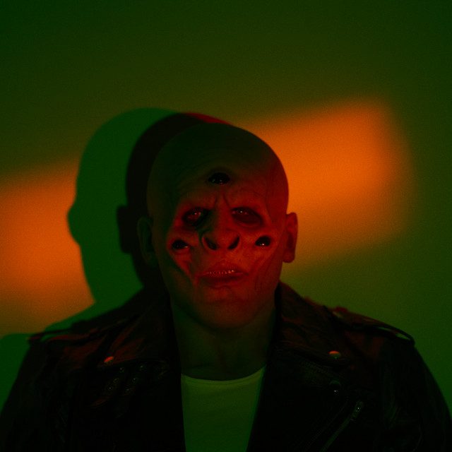 A photo of an individual with multiple eyes in a leather jacket and white t-shirt.