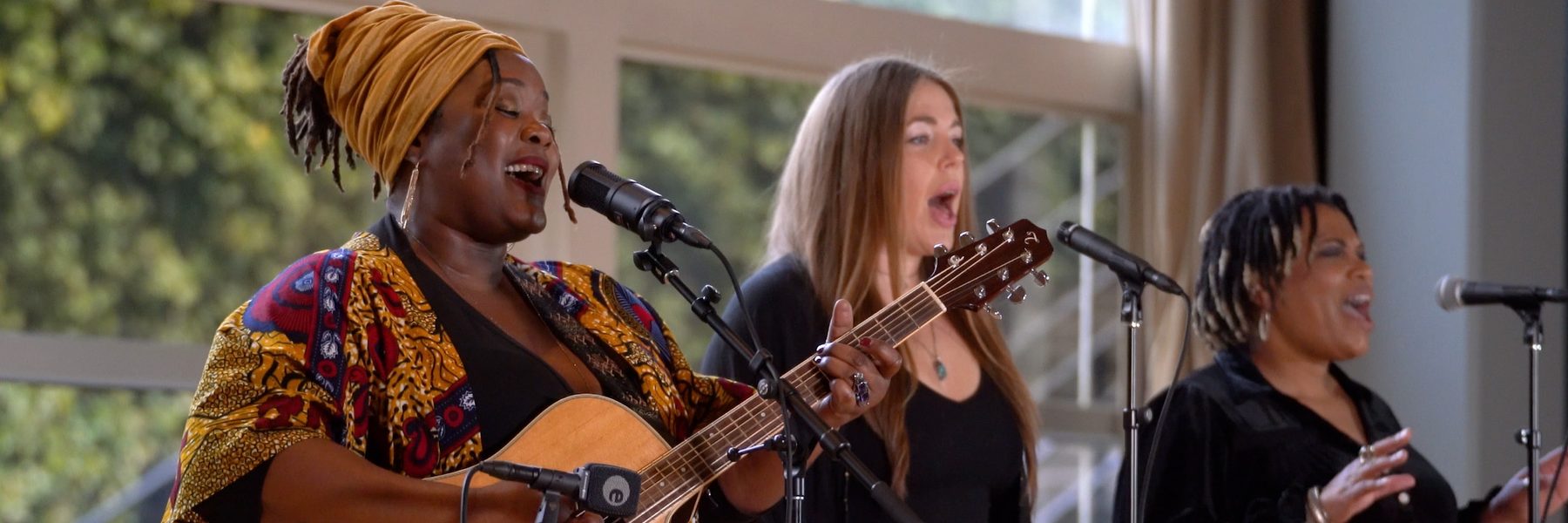 Picture image of klyshona performing with guitar into microphone and two other singers to the right of her
